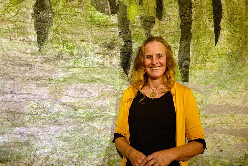 Eine lächelnde Frau steht vor einem grünen  Papier-Gobelin gefertigtem, grünem Gemälde