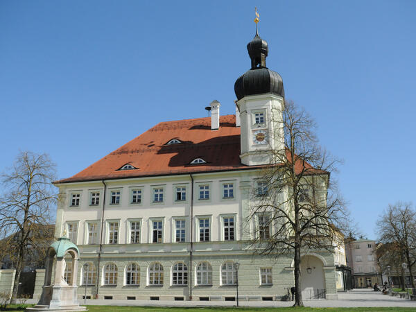 Dreigeschössiges historisches Gebäude mit rotem Spitzdach und einem kleinen Glockenturm