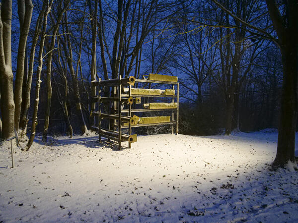 Nachaufnahme: Ein Scheinwerfer erhellt eine Kunstskulptur in Form eines Stahlregals. Am Boden liegt Schnee.
