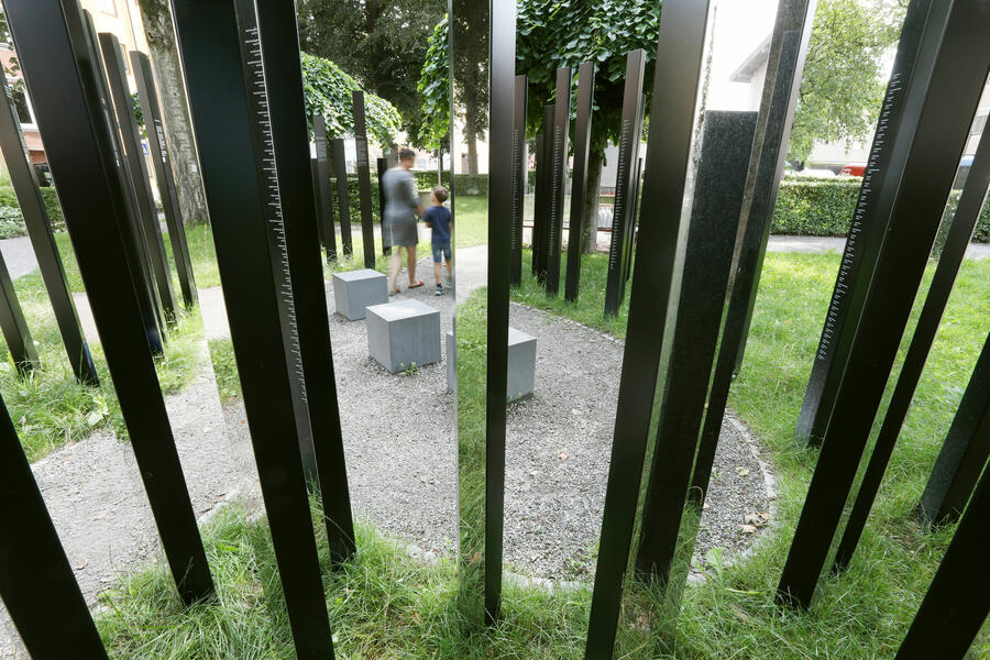 Ein kleiner Kiesplatz ist umrandet von vielen aus dem Boden ragenden Metallbalken. Auf den Balken sind 742 Namen eingraviert, zum gedenken an die Opfer des NS-Regimes.