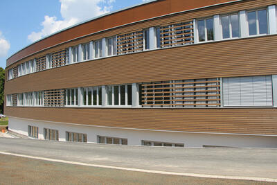 Außenaufnahme eines modernen Klinikgebäudes mit Holzverrkleidung bei Sonnenschein und weiß-blauem Himmel.