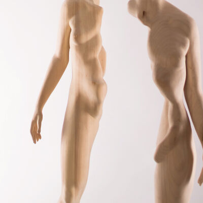 Zwei Aktskulpturen aus Holz, die mit Abstand aufgestellt sind. Sie zeigen jeweils eine Körperhälfte eine Mannes und einer Frau. Die männliche Hälfte trägt den Kopf.
