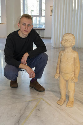 Junger Mann kniet negen der Figur eines Kindes aus Holz