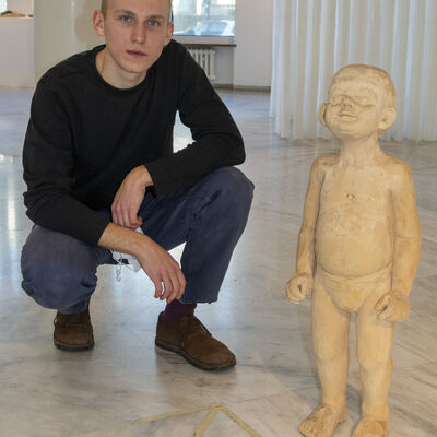 Junger Mann kniet negen der Figur eines Kindes aus Holz