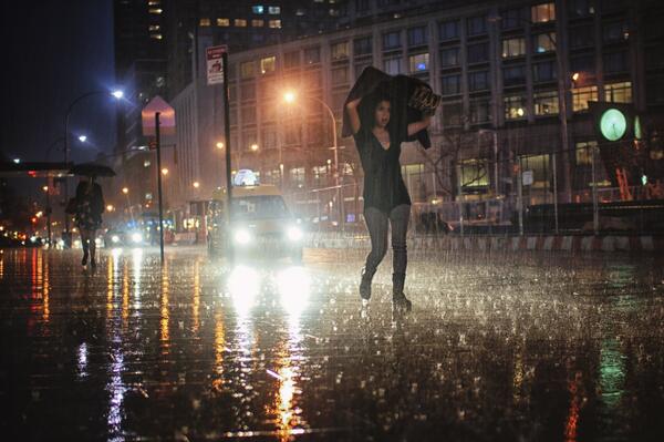 Kunstwerk: Fotografie einer Frau, die durch den Regen läuft und dabei eine Jacke über dem Kopf hält