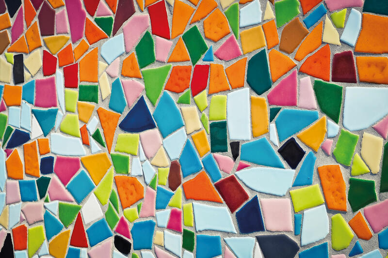 Wandausschnitt mit vielen unregelmäßigen Mosaiksteinchen in verschiedenen Farben