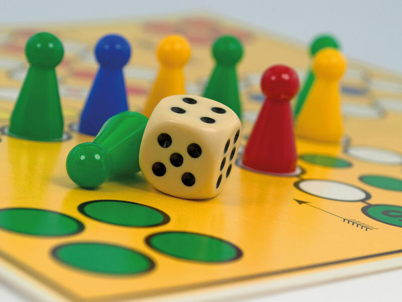 Ausschnitt eines Mensch-ärgere-dich-nicht-Spiels mit einem Würfel und Spielsteinen in grün, blau, gelb und rot