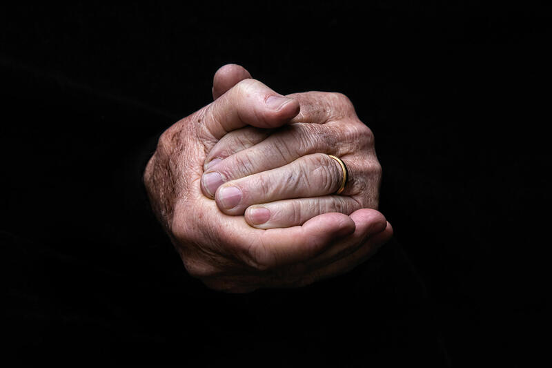 Foto mit ineinandergelegten Händen einer älteren Person, die einen Ehering an der linken Hand trägt