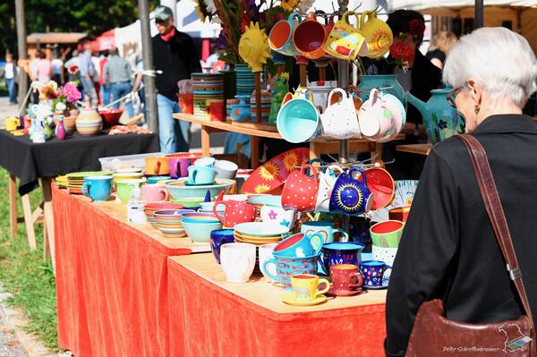 Eine Frau betrachtet einen bunten Marktstand mit Töpferware 
