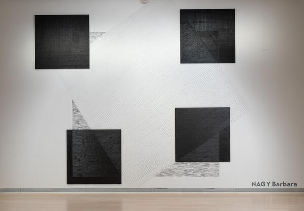 Kunstwerk: An einer Wand hängen vier große quadratische, sehr dunkel gebeizte Holztafeln. Diese werden durch Kratzspuren an der Wand miteinander verbunden. Diese Spuren bilden weitere, große Quadrate.