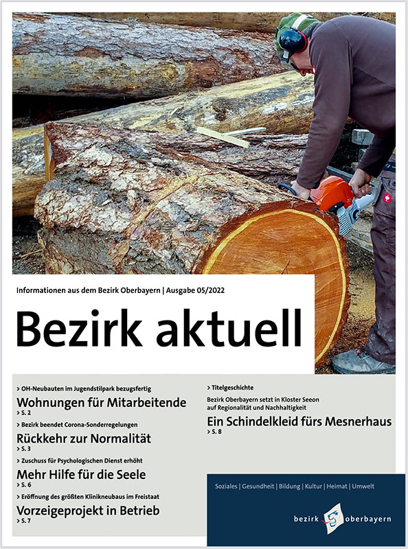 Coverbild von Bezirk aktuell mit einem großen Holzstamm, von dem eine Person mit einer Motorsäge eine Scheibe abschneidet.