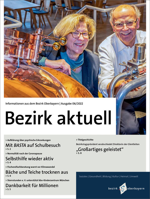 Coverbild von Bezirk aktuell mit einer Mann und einer Frau, die hinter Kupferkesseln in einer Brauerei Knieen und ins Bild lachen.
