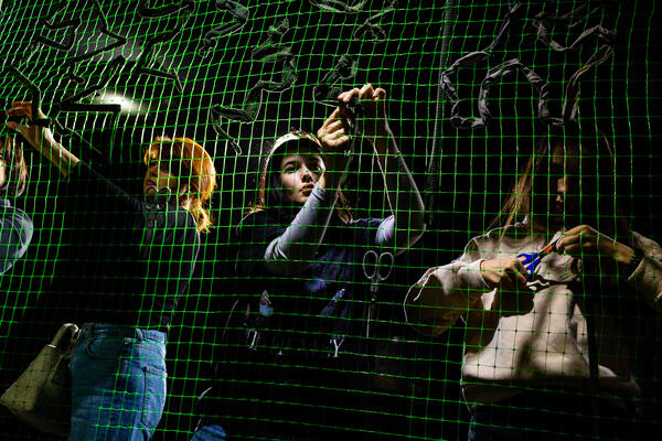 Kunstwerk: Die Fotografie zeigt mehrere Personen, die ein Tarnnetz flechten