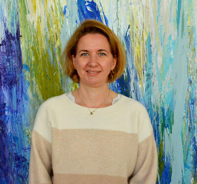 Frau in beigen Pullover steht vor einem blau-grünen abstrakten Gemälde