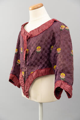 Foto einer lila rot karierten Trachtenjacke mit Blumenstickerei. 