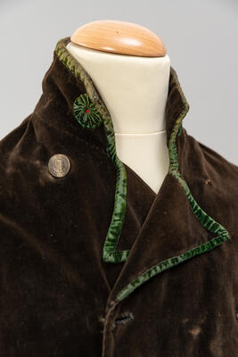 Foto einer braunen Jacke aus Samt mit Stehkragen und grünen Details am Kragen.