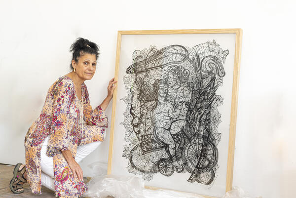 Eine Frau kniet neben einem Kunstwerk. Dabei handelt es sich um einen mit einem Holzrahmen versehenen Scherenschnitt.