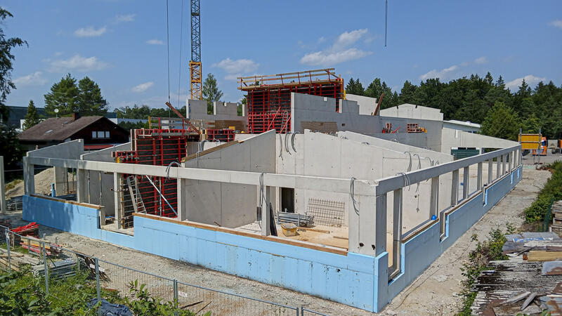 Foto einer Baustelle: Betonwände und Stützen. Im Hintergrund Betonschalungen. Auf Bodenhöhe hellblaue Isolierungsplatten.