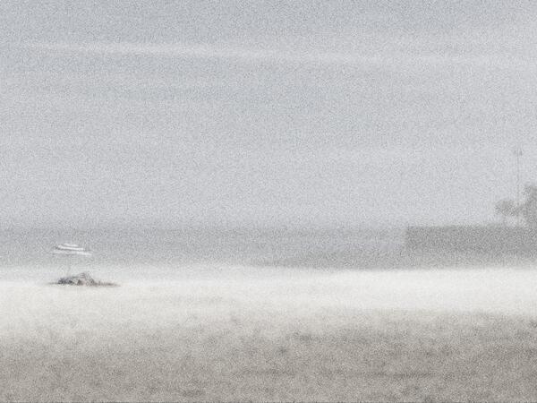 Graues, verpixeltes Foto von einem Strand. Links ist ein Sonnenschirm zu erkennen und rechts ein Gebäude und eine Palme.