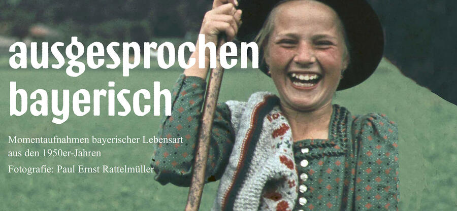 Rechts auf dem Bild steht "ausgesprochen bayerisch - Momentaufnahmen bayerischer Lebensart aus den 1950er Jahren". Links ist ein junges Mädchen zu sehen, dass einen Wanderhut, einen Stock in der Hand hält und herzhaft lacht.