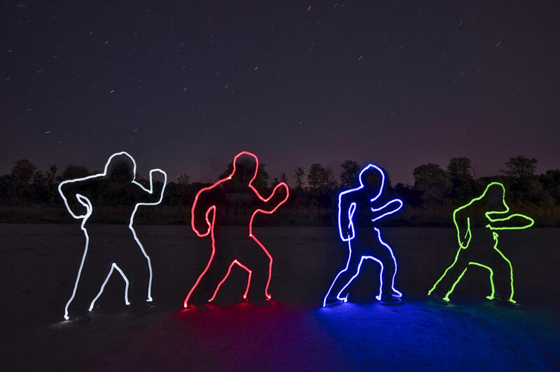 Nachtaufnahme: In der Landschaft beleuchten Lichtspuren die Umrisse von vier Figuren