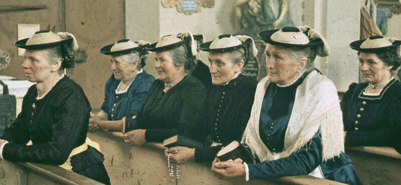 Historisches Foto in verblichenen Farben aus den fünfziger Jahren: Frauen in Tracht knien zwischen den Bänken in einer Kirche. Manche haben ein Gebetsbuch oder eine Gebetskette in der Hand. Alle Frauen tragen die Haare in einem Dutt, tagen ähnliche Trachten und haben den gleichen Hut auf.