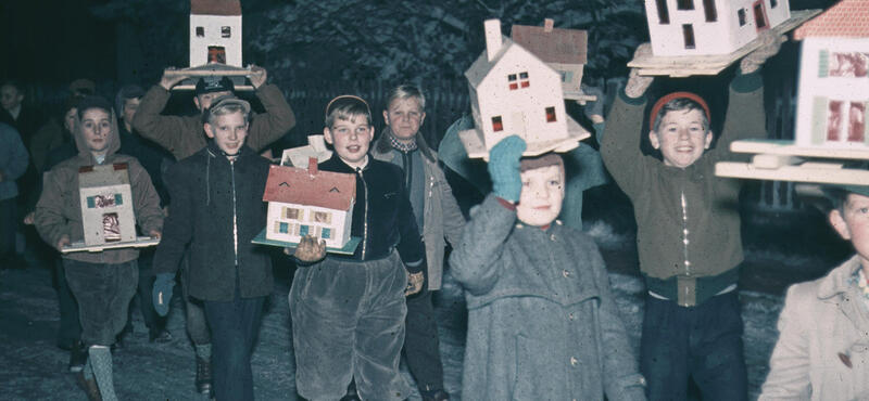 Historisches Foto in verblichenen Farben aus den fünfziger Jahren: Kinderscharr laufen im dunkeln und manche tragen kleine Häuser in den Händen. im Hintergrund ist ein Gartenzaum: