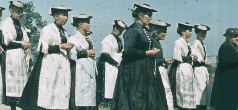 Historisches Foto in verblichenen Farben aus den fünfziger Jahren: Frauen gehen in Viererreihen hintereinander her. Sie haben alle die gleiche Tracht an und haben ihre Haare zu einem Dutt zusammengebunden.  Und sie tragen alle den gleichen Hut. Ihre Hände haben sie zusammengefaltet.