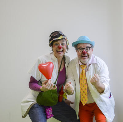 EIn Mann und eine Frau sind als Clowns verkleidet und lachen den Betrachter an