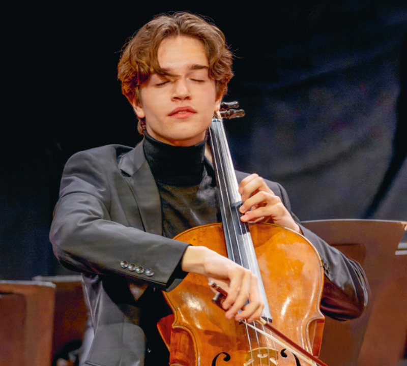 Junger Mann im Anzug spielt mit geschlossenen Augen ein Cello