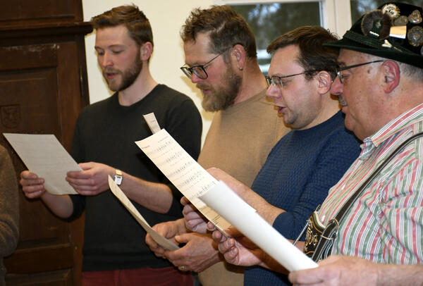 Vier Männer singen mit einem Liedblatt in der Hand;
