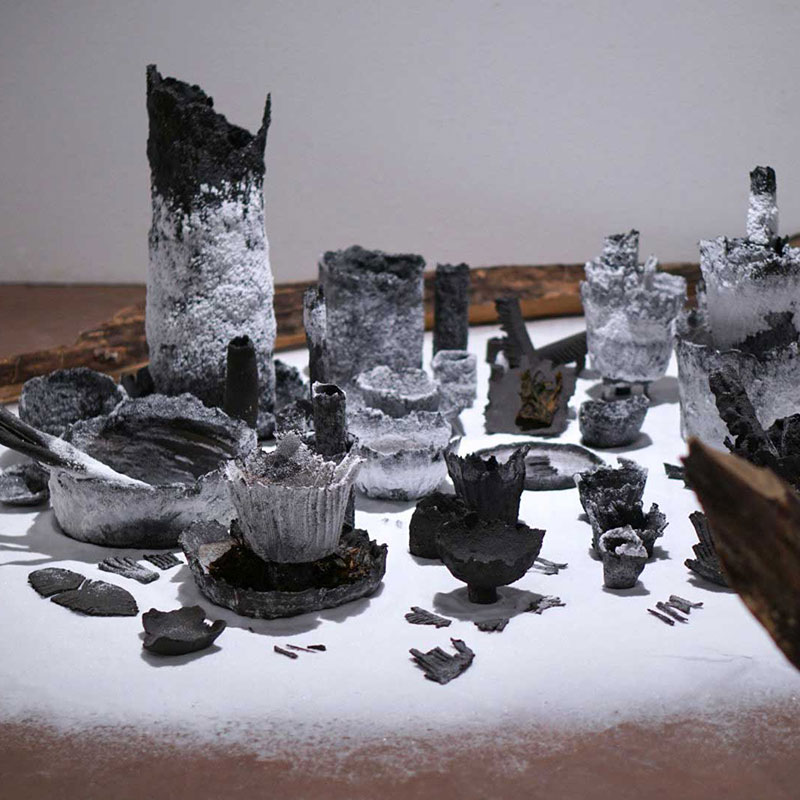 Kunstwerk: Viele schwarzgebrannte Keramikobjekte sind auf einer hellen Unterlage angeordnet.