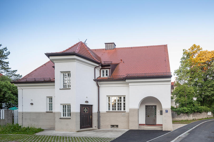 Ein großes Haus mit roten Dachziegeln und einem eckigen Turm mit einer dunkelbraunen Holztür.