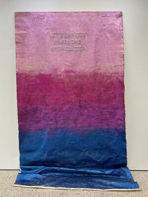Ein Teppich, der an der Wand hängt. Er hat einen Farbverlauf von oben nach unten in den Farben hellrosa, pink, lila, dunkelblau.