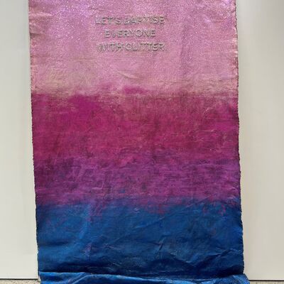 Ein Teppich, der an der Wand hängt. Er hat einen Farbverlauf von oben nach unten in den Farben hellrosa, pink, lila, dunkelblau.