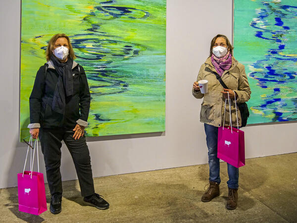 In einem Ausstellungsraum, an dessen Wänden großformatige Kunstwerke hängen, stehen zwei Besucherinnen mit FFP2-Gesichtsmasken. 