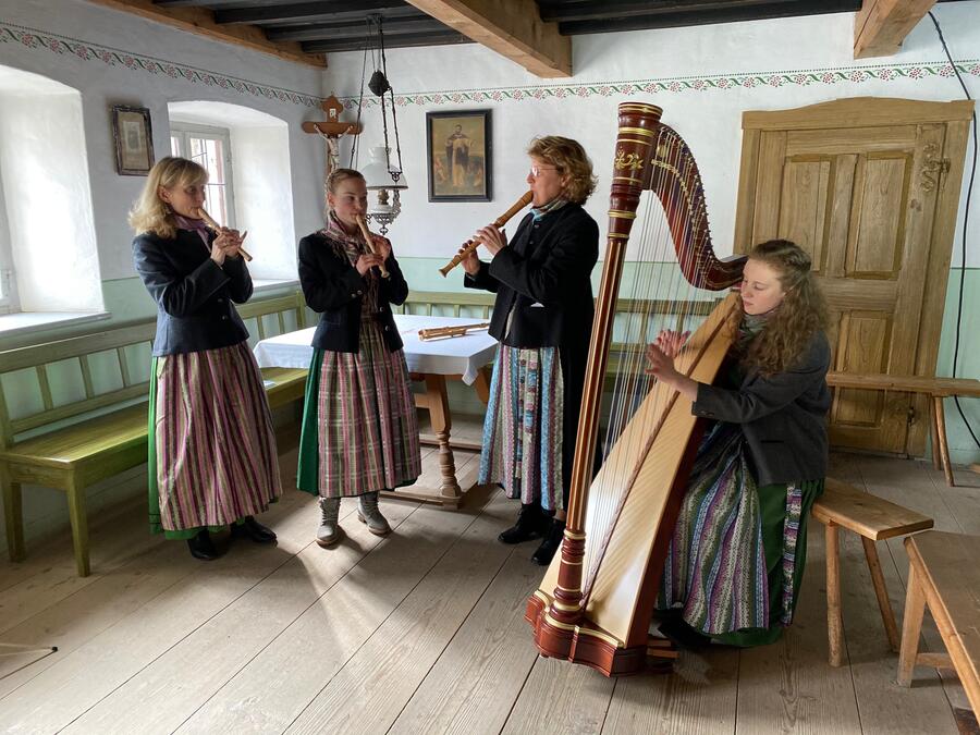 Vier Frauen stehen in einem bayerischen Raum. Drei Frauen in Dirndl spielen Blockflöte und eine jüngere Frau spielt Harfe.