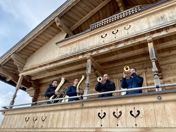Ein traditionelles Fachwerkhaus. Auf dem Balkon im ersten Stock stehen vier Männer mit Blasinstrumenten und spielen.
