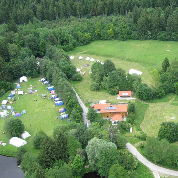 Luftbild auf das Gelände der Jugendsiedlung Hochland mit Wald, Wiesen, Häusern und einem Zirkuszelt