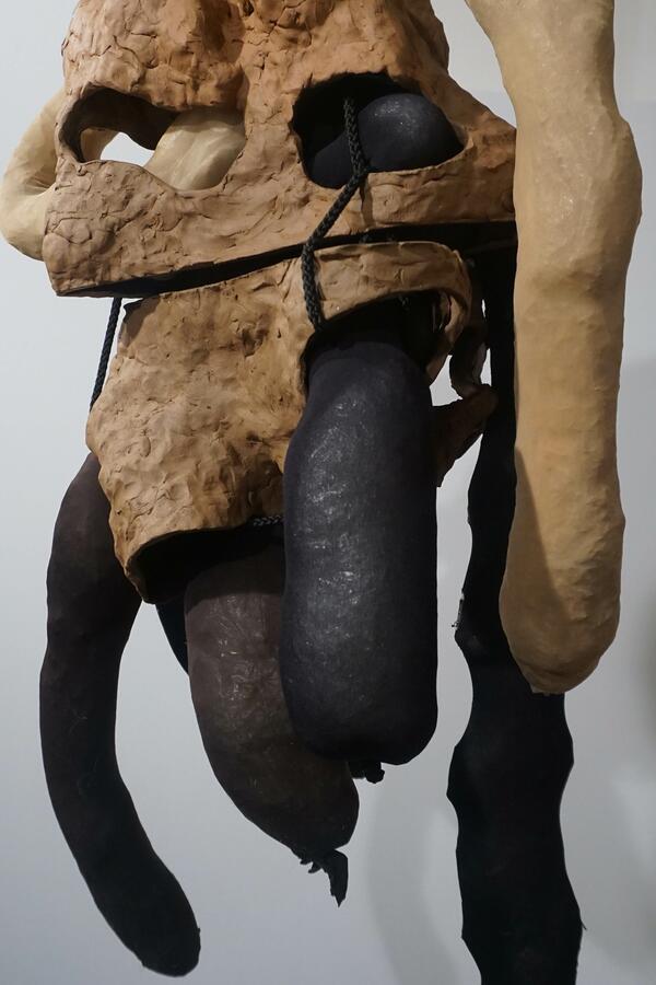 Eine Skulptur aus Keramik, an der mehrere längliche gefüllte Nylonstrümpfe hängen. 
