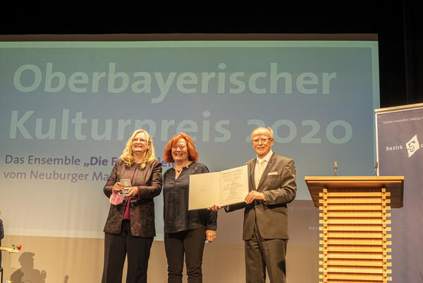 Zwei Frauen erhalten von einem Herrn eine Urkunde mit dem Oberbayerischen Kulturpreis