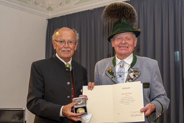 Zwei Männer, einer in einem Trachtenanzug und einer in Tracht, Hut und Gamsbart, halten Urkunde und Medaille