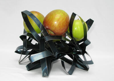 Skulptur aus gebogenen Metallschleifen mit drei Äpfeln

