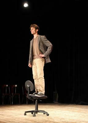 Ein Mann steht auf einer Bühne auf einem Büro-Stuhl 